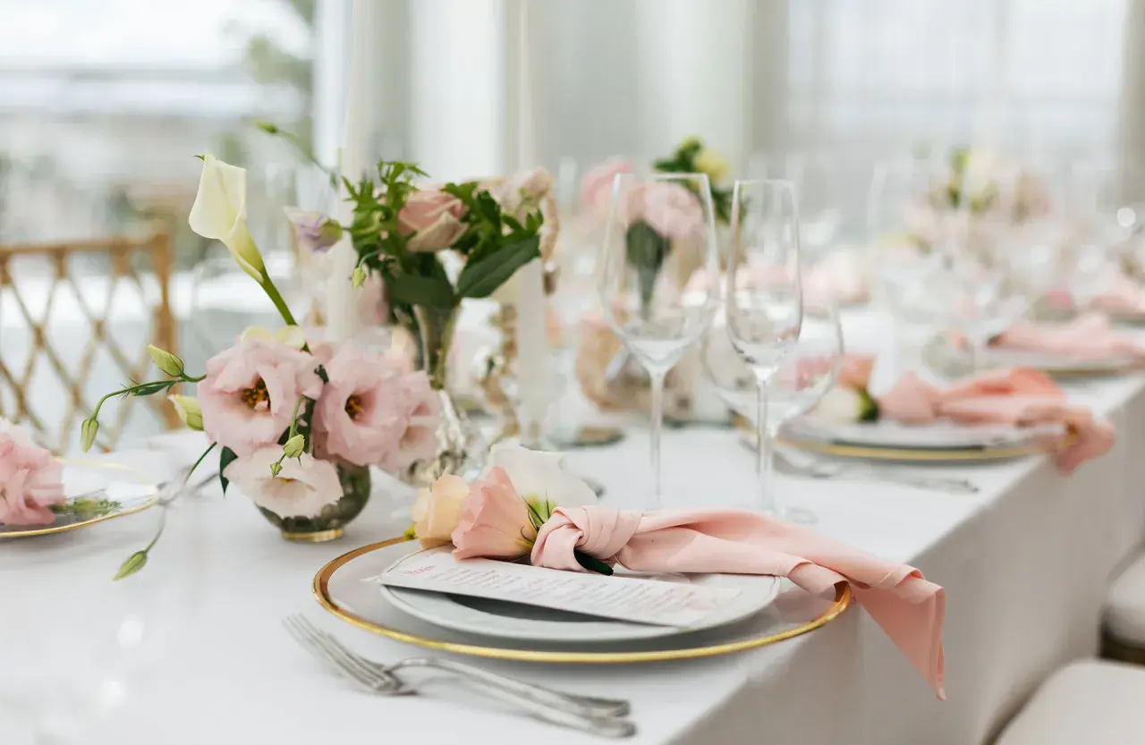 Ett vackert dukat bord med rosa dekorationer, blommor och glas. En elegant dukning för ett speciellt tillfälle.