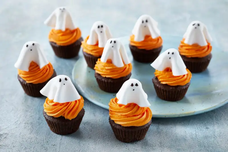 Sju chokladmuffins med orange frosting och vita spökdekorationer. Perfekt att baka till Halloween med barnen!