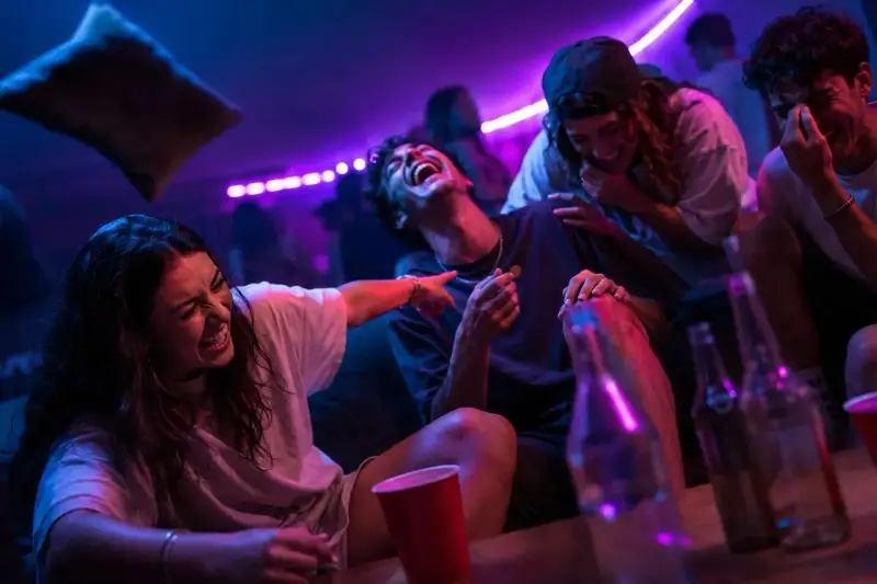 Ungdomar skrattar och har kul på en fest, kanske med kluriga gåtor till festen. Ljusen är lila och blå.