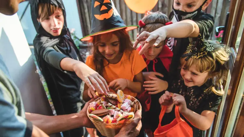 Barn i Halloween-kostymer sträcker sig efter godis ur en korg. Det är en klassisk "bus eller godis"-kväll!