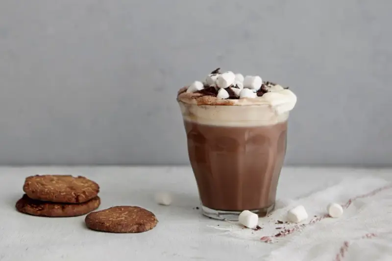 En härlig varm choklad med choklad, toppad med marshmallows och chokladspån. Bredvid står några chokladkakor.