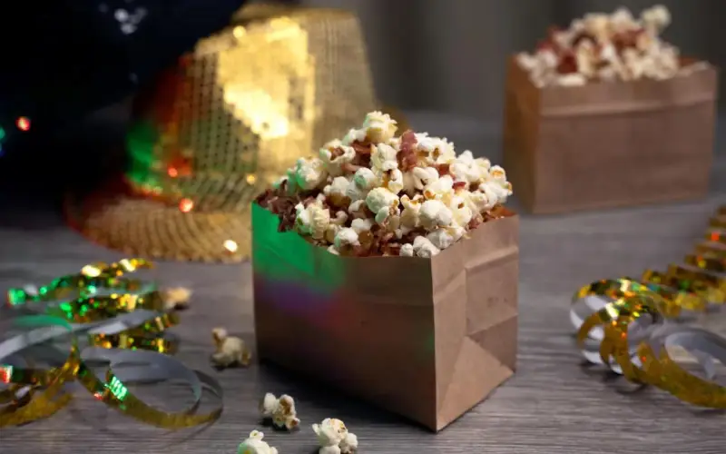 Festliga popcornboxar med bacon, redo för nyårsfirande. Glitterband och en paljetthatt i bakgrunden skapar en festlig stämning.